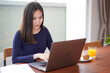 © Freedomz - Young asian woman eating bread with a glass of orange juice while looking on laptop screen to typing