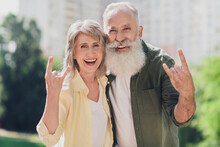 Photo Of Funky Cool Senior Couple Wear Casual Clothes Walking Showing Hard Rock Sign Smiling Outside Urban City Street