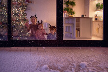 Snow Flakes Falling On The Patio At Magical Chrismas Night, With Happy Kids Watching It At The Background