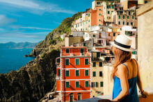 Young stylish woman looking at panoramic view of Riomaggiore colorful village, Cinque Terre, Italy