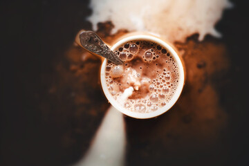 Top view of a mug of hot fragrant cocoa, into which cold milk is poured. The process of making a delicious drink in the morning. A mess.