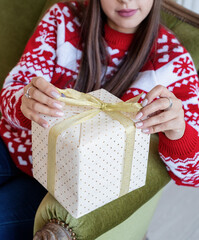 Young woman in red sweater wrapping a gift sitting on the couch