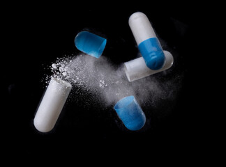 white and blue pill with exploding over a black background,Concept of medicine