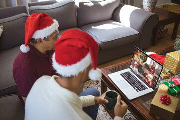 Canvas Print - Biracial father and adult son in santa hats making laptop christmas group video call with friends