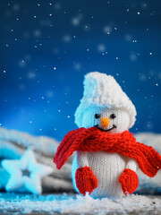 Wall Mural - Knitted toy snowman in a hat, mittens and scarf. Blue background with falling snow