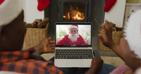 Canvas Print - African american couple with santa hats using laptop for christmas video call with santa on screen