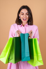 Wall Mural - Portrait of a young woman in a pink dress on a beige background with glitter makeup holding shopping packages cute excited