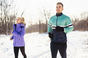 Young couple in sportswear doing morning exercise at snowy forest. Fitness, sport and healthy lifestyle concept. 