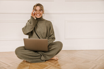 attractive young caucasian woman is sitting on floor with laptop computer on lap in bright room. gir