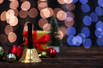 Golden Christmas bell and decorations on wooden table against blurred lights