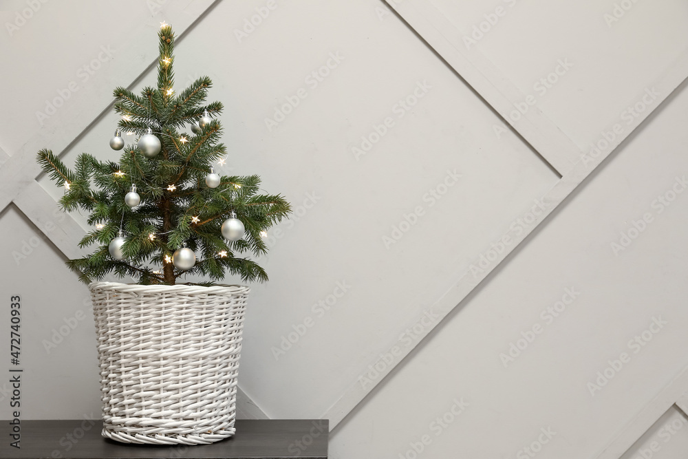 Beautiful decorated Christmas tree in pot on table near light wall