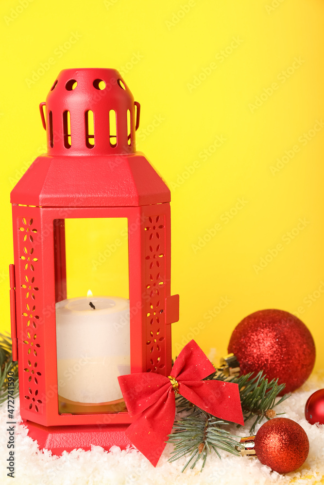 Christmas lantern with burning candle, balls and snow on yellow background