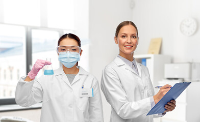 Canvas Print - medicine, science and healthcare concept - happy smiling female doctors or scientists in white coats with clipboard and test tube over medical office at hospital on background