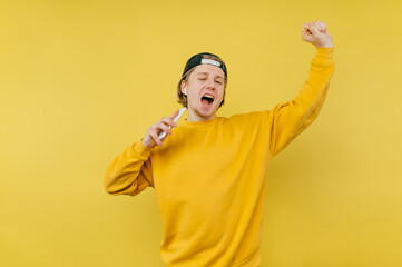 Wall Mural - Joyful guy in a cap and a yellow sweatshirt listens to music in wireless headphones and dances with a smartphone in his hands.