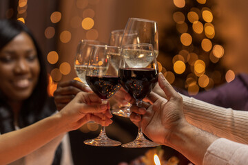 holidays, party and celebration concept - multiethnic group of happy friends having christmas dinner at home and drinking wine