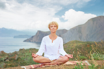Wall Mural - Senior woman doing yoga exercises with mountain on the background
