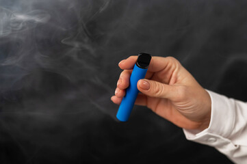 Caucasian woman smokes disposable vape on black background. Alternative device for smoking. Close-up of a female hand.