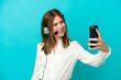 © luismolinero - Telemarketer English woman working with a headset isolated on blue background making a selfie
