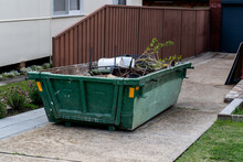 Skip Bin With Household Waste Rubbish On A Front Yard. House Clean Up Concept.