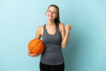 Sticker - Young woman playing basketball isolated on blue background pointing to the side to present a product