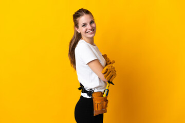 Wall Mural - Young electrician woman isolated on yellow background with arms crossed and looking forward