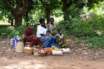 West African farmer's wife and children sitting on the edge of a dirt road waiting for customers to buy their home grown products