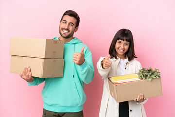 Wall Mural - young beauty couple moving in new home among boxes isolated on pink background giving a thumbs up gesture because something good has happened