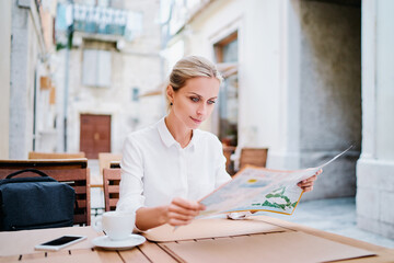 Wall Mural - Happy tourist drinking coffee. Pretty young woman with map sitting at table at old town cafe, outside. Travel by Europe.