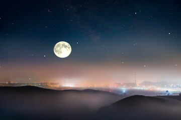 Wall Mural - foggy night city light bokeh ,mountains on sunset orange evening starry blue night sky big bright mo
