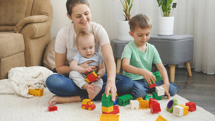  Little baby boy and older brother playing with mother in toys on carpet in living room. Concept of family having time together and children development