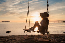 Young Woman Sitting On Swing Over Sea At Sunset