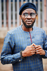 Wall Mural - African guy in blue authentic costume, eyeglasses and beret. Fashionable nigerian man.