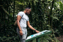 Young Black Male Traveler Searching Route On Information Sign In Forest