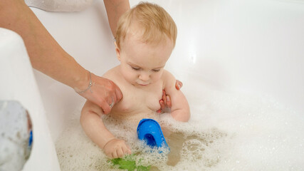 Wall Mural - Little concentrated baby boy playing with toy ships and boat in bathroom while washing