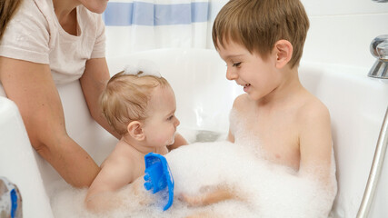 Wall Mural - Cute baby boy and older brother washing and playing in bath with foam. Concept of children hygiene, healthcare and family care at home