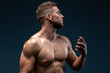 Horizontal view of the handsome muscular guy using cologne or perfume while posing isolated on black background. Man showing his strong body and muscles