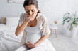 © LIGHTFIELD STUDIOS - young pregnant woman feeling nausea and covering mouth in bedroom.