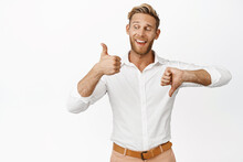 Yes Or No. Smiling Blond Man Showing Thumbs Up And Thumbs Down, Weighing Decision, Standing Over White Background