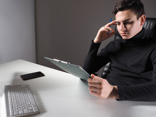 Poster - Thoughtful man sitting in an office chair. Man looks at the documents and thinks. Businessman thinks about his company. Guy with a tablet and pen passes the test. Testing when applying for a job.
