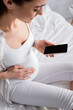 © LIGHTFIELD STUDIOS - blurred and happy pregnant woman holding smartphone with blank screen.