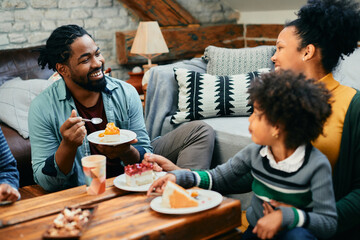 Wall Mural - Happy black family enjoys while eating cake and talking at home.