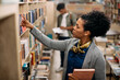 © Drazen - African American mid adult student takes book from shelf at university library.