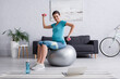 © LIGHTFIELD STUDIOS - cheerful pregnant woman exercising on fitness ball with dumbbells near laptop.