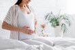© LIGHTFIELD STUDIOS - partial view of cheerful pregnant woman touching belly in bedroom.