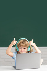 Fototapete - Cute boy with thumbs up wearing headphones, study with laptop in classroom, listening audio lesson course. First day at school.