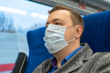 Wall Mural - Portrait of male passenger wearing medical face mask in public transportation. Millennial man looking away at window, thinking, going to home by train during coronavirus pandemic. New normal