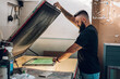 © Zamrznuti tonovi - Male worker using a screen exposure unit while working in a printing workshop