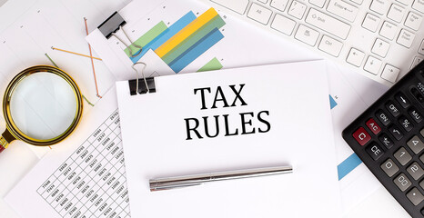 Poster - TAX RULES text on the white paper on the light background with charts paper ,keyboard and calculator