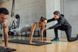 © BASILICOSTUDIO STOCK - Personal trainer corrects woman's plank position at gym.