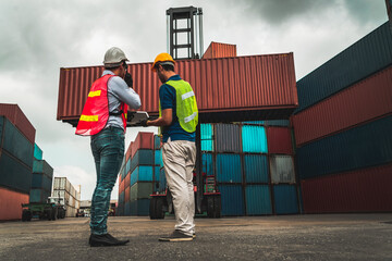 Wall Mural - Industrial worker works with co-worker at overseas shipping container yard . Logistics supply chain management and international goods export concept .